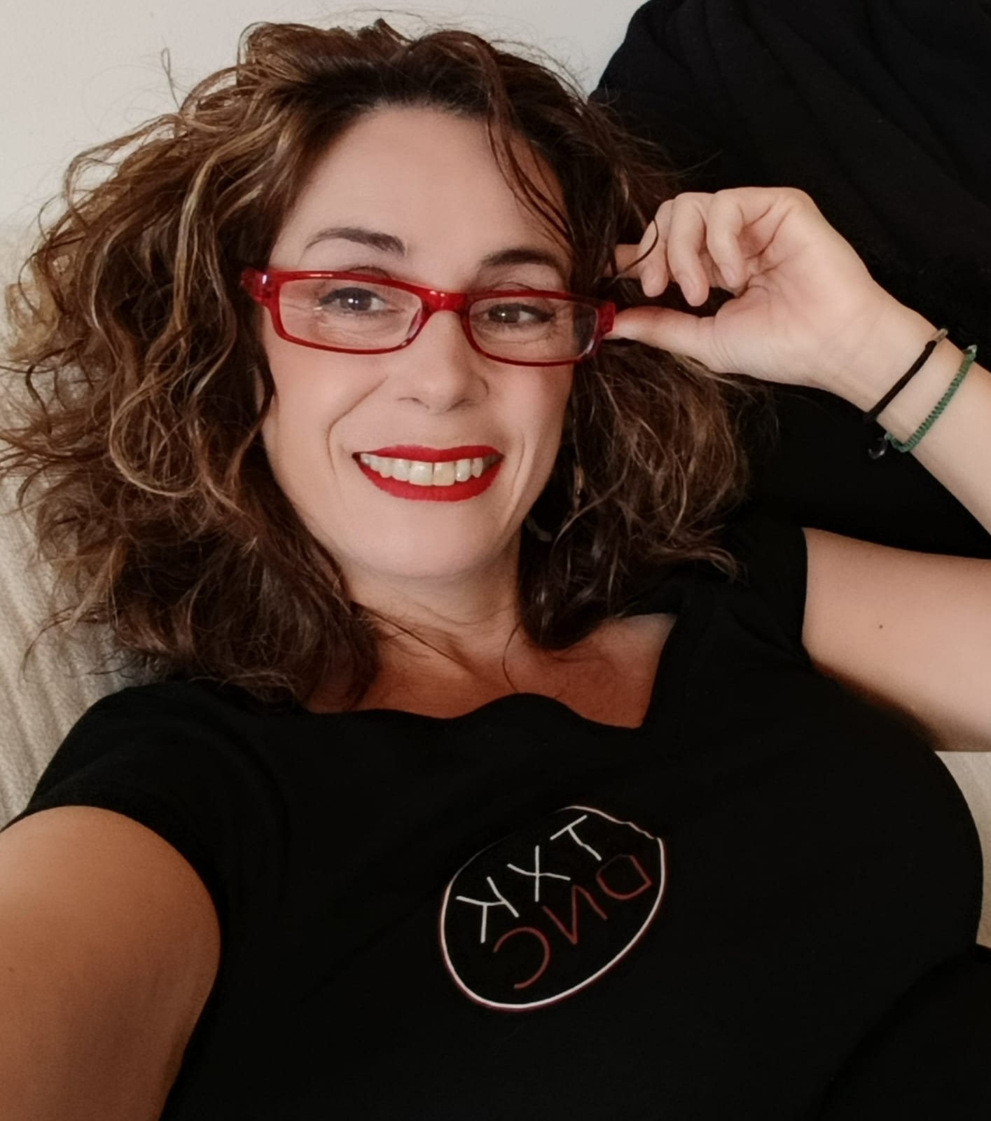 Mujer de cabello rizado abraza a un hombre con ojos cerrados en un evento, fondo desenfocado.
